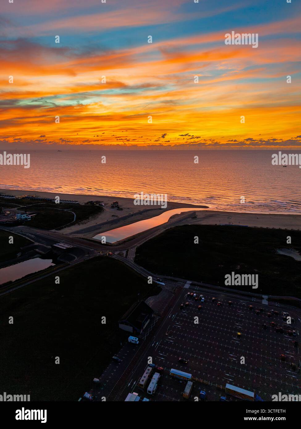 Vista aerea del tramonto costiero con il cielo dorato sulla tranquilla spiaggia di sabbia e sul canale dell'oceano si incontrano con il parcheggio strutturato e le strade, che fondono bellezza naturale Foto Stock