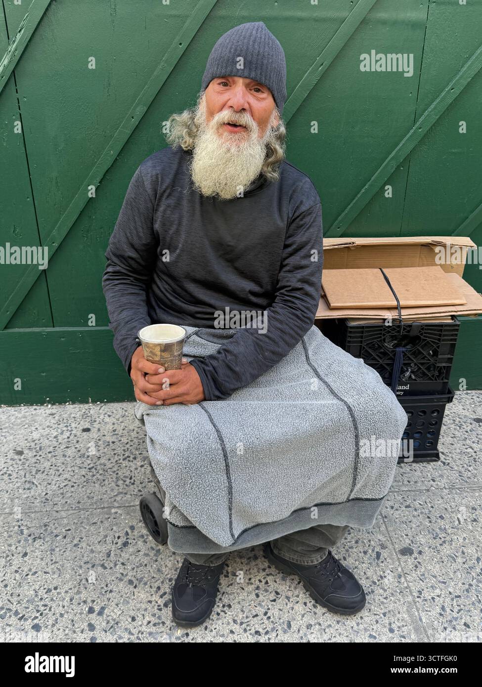 Un uomo dall'aspetto tranquillo con una tazza che chiede donazioni si trova lungo Park Avenue a Manhattan, New York. Foto Stock