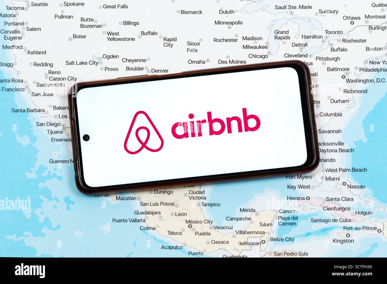 Primo piano di uno smartphone con logo airbnb rosa sopra una mappa politica del messico e degli stati uniti Foto Stock