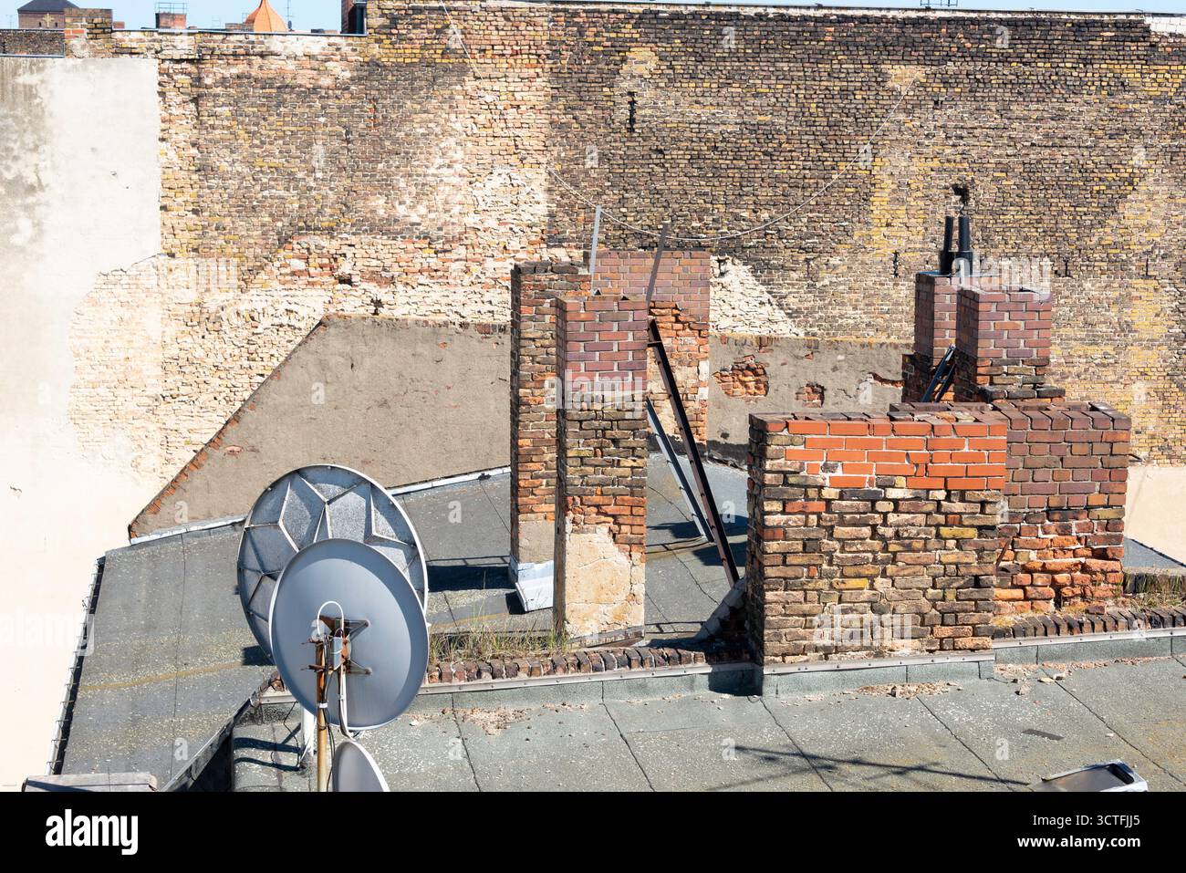 Una vista grintosa e strutturata sui vecchi tetti di Berlin-Kreuzberg. Pareti in mattoni in decadenza e camini in rovina contrastano con le moderne parabole satellitari, crea Foto Stock
