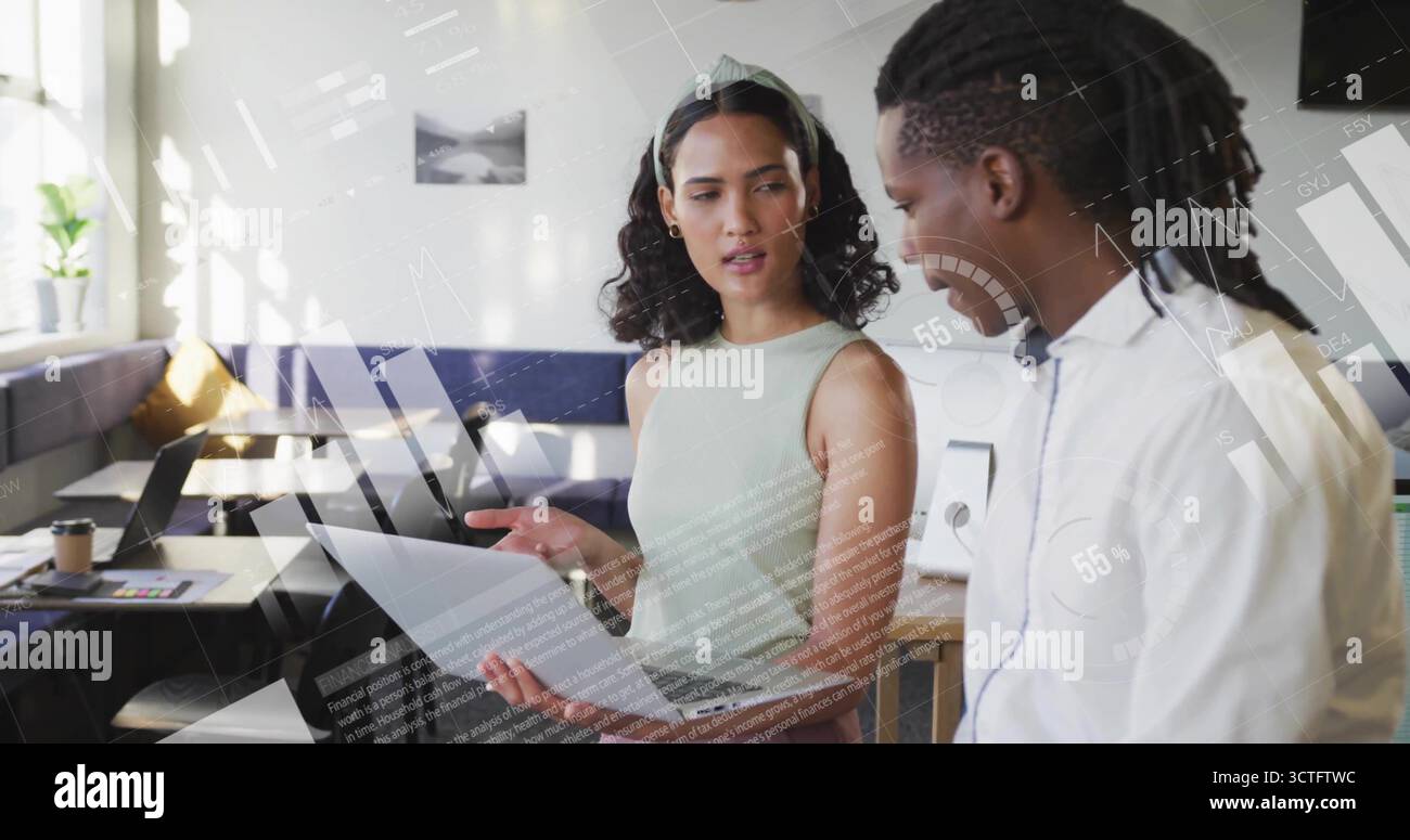 Colleghi in piedi in un abbigliamento informale per affari che discutono documenti in ufficio, con un computer portatile e un caffè Foto Stock