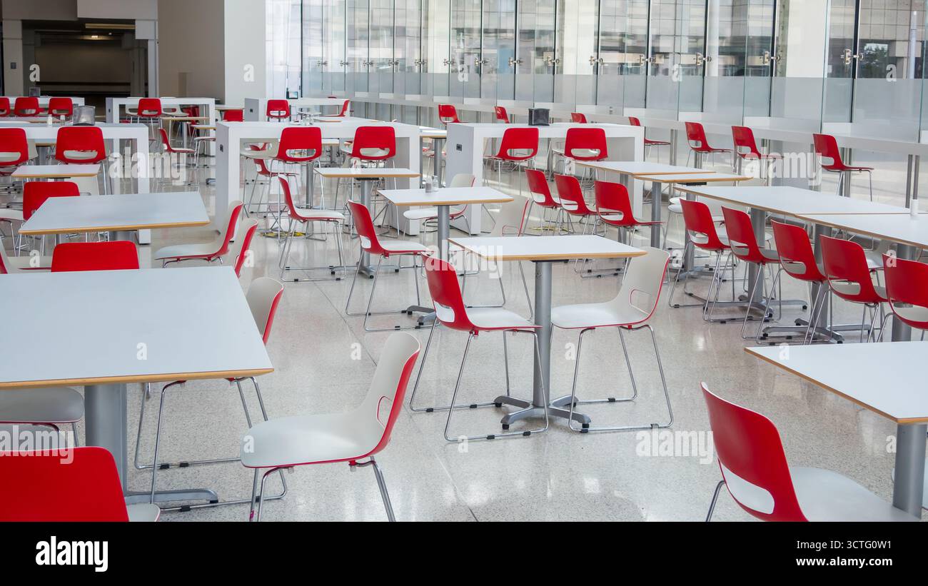 Caffetteria vuota con sedie rosse e tavoli bianchi in un edificio di vetro laterale. Foto Stock
