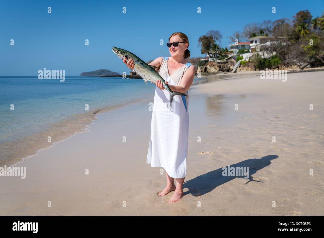 Donna matura felice che mostra pesce appena pescato su una spiaggia di Contadora Island, Panama Foto Stock
