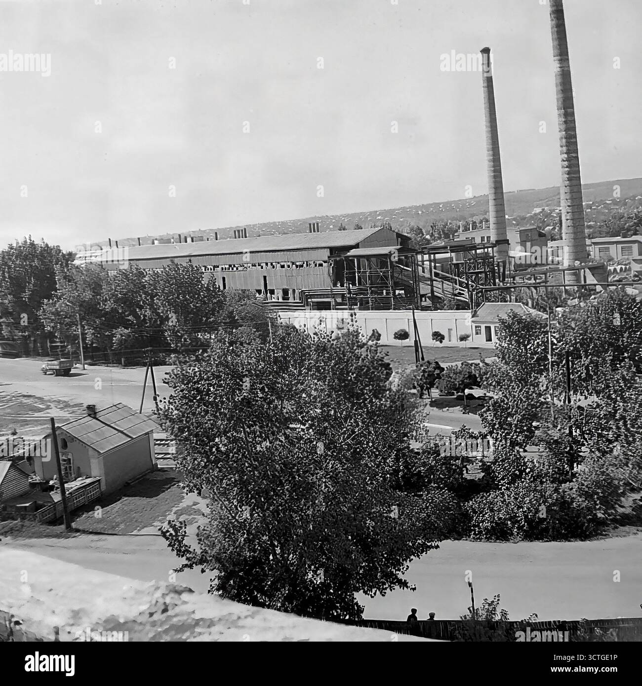 Un paesaggio industriale a Sloviansk, RSS Ucraina, durante gli anni '1970 Questa fotografia d'archivio mostra una grande fabbrica o un impianto di lavorazione, probabilmente un complesso di elevatore di grano, che domina il distretto. Due massicce aree affumicate si innalzano in alto sopra l'edificio principale, simboleggiando il potere industriale della regione del Donbas. In primo piano, le strade residenziali con auto come la classica Moskvitch-412 coesistono con la zona industriale. Questa immagine cattura la tipica pianificazione urbana dell'era sovietica, dove la vita industriale e residenziale era strettamente intrecciata Foto Stock