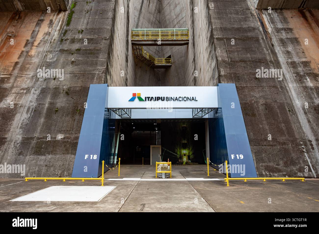 Itaipu Binacional, Brasile - 22 giugno 2025: Il cancello di accesso centrale e la segnaletica Itaipu Binacional sotto il massiccio muro della diga della centrale elettrica. Foto Stock
