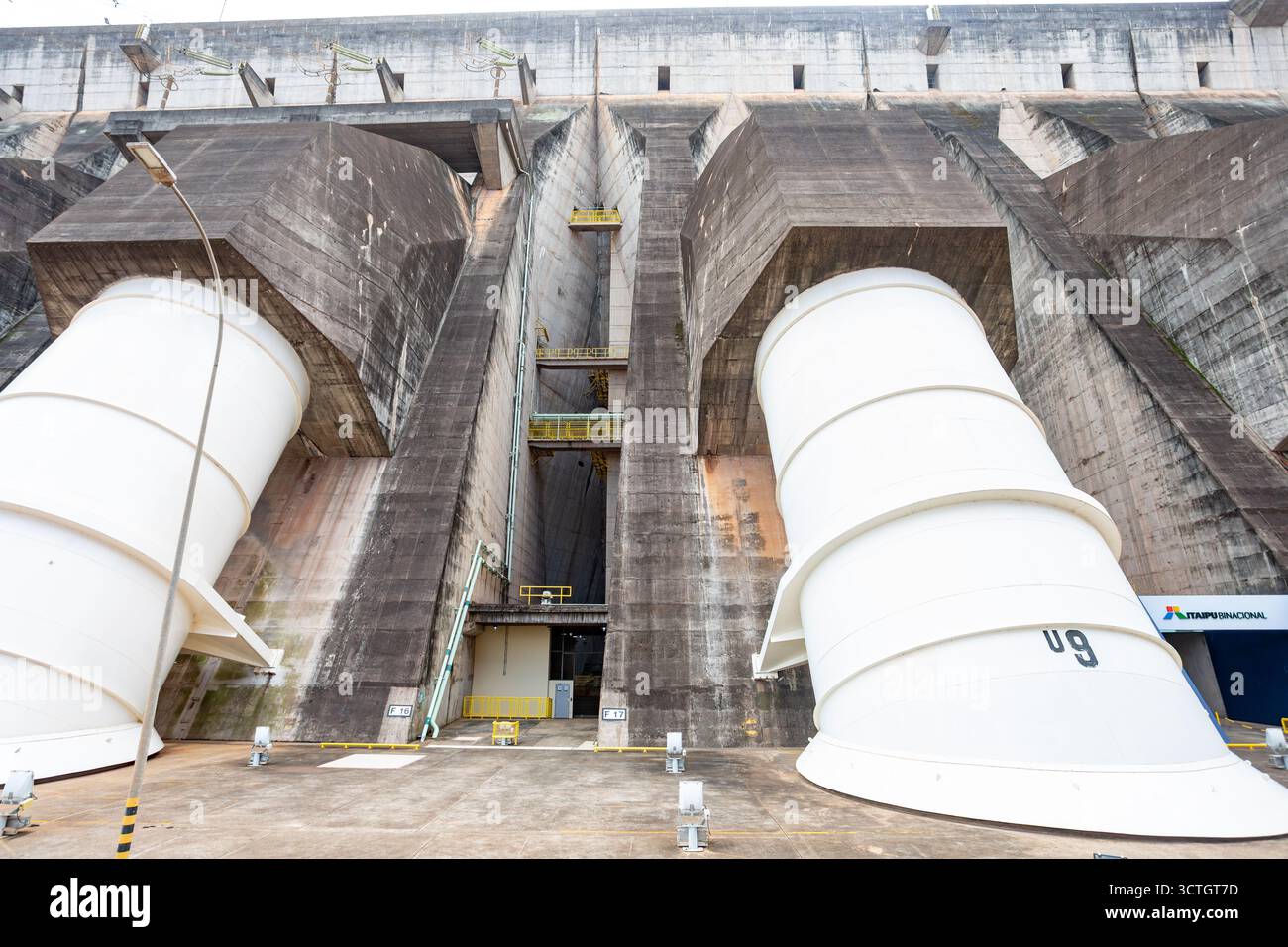 Itaipu Binacional, Brasile - 22 giugno 2025: Vista ravvicinata dei tubi di pescaggio delle turbine bianche giganti che emergono dalla massiccia faccia in cemento dell'Itaipu D. Foto Stock