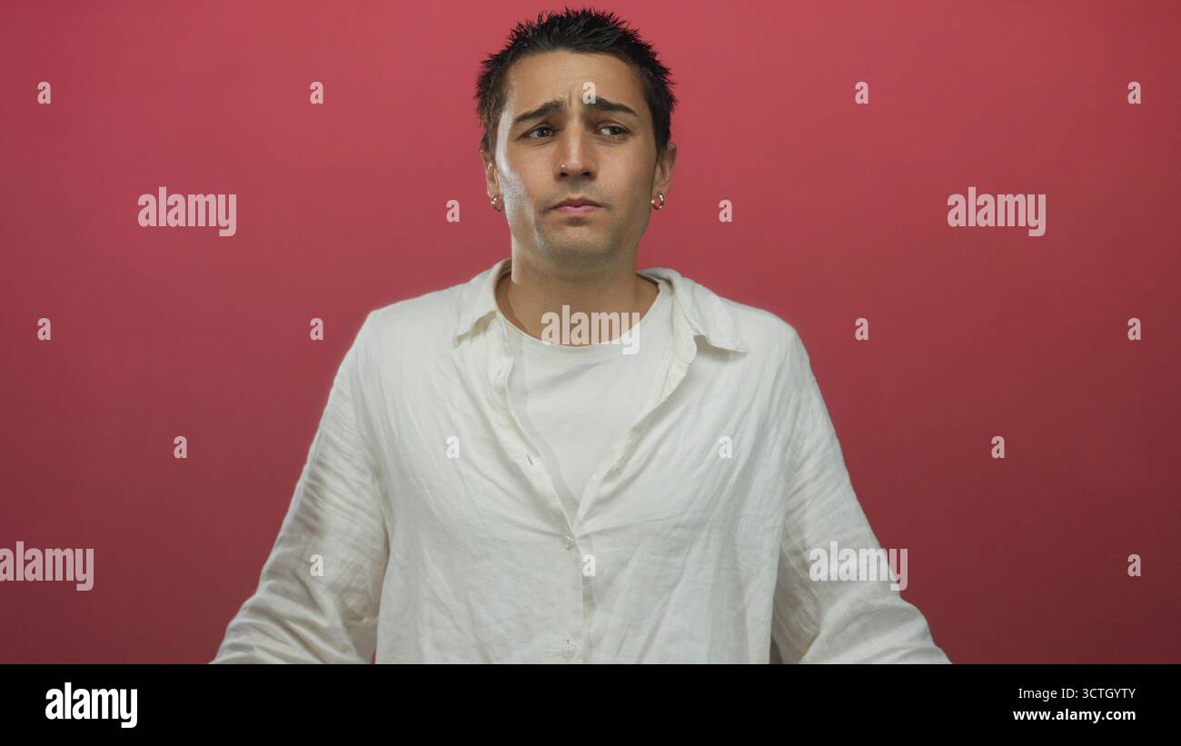 Giovane uomo in camicia bianca si staglia su sfondo rosso mostrando espressione emotiva a occhi chiusi Foto Stock