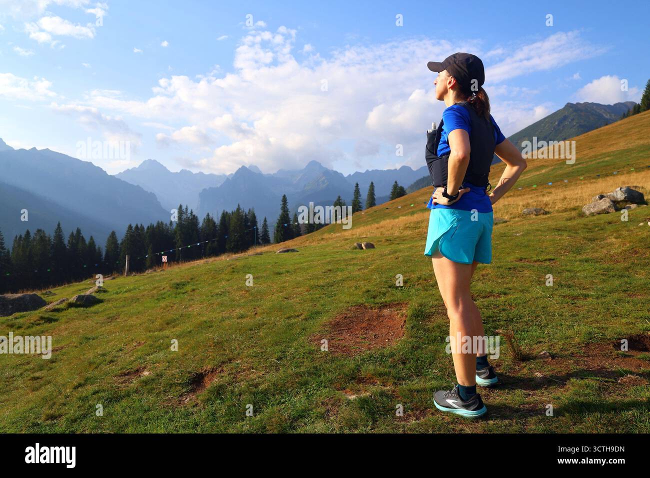 Una donna runner gode della vista delle montagne mentre riposa durante una corsa su una roccia. Foto Stock
