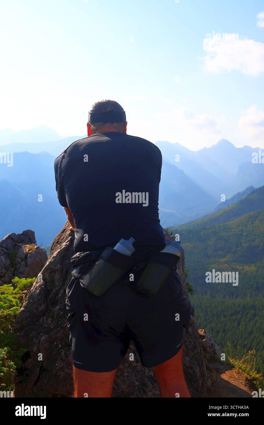 Uomo corridore che gode della vista sulle montagne con bottiglie d'acqua sulla schiena Foto Stock