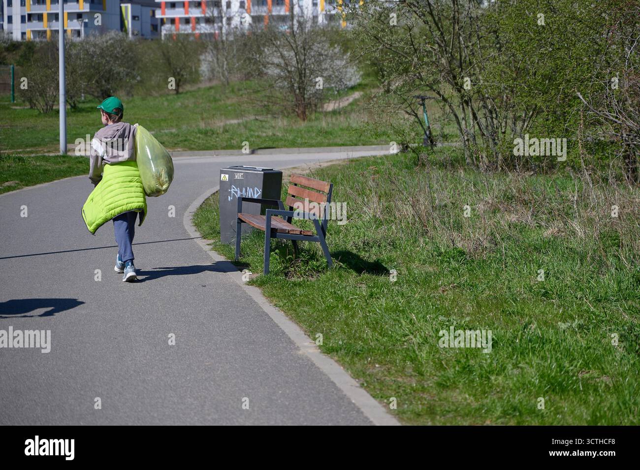 Donna che trasporta una borsa verde per la spazzatura che cammina sul percorso del parco durante la pulizia ambientale, vista posteriore a tutto il corpo alla luce di mezzogiorno Foto Stock