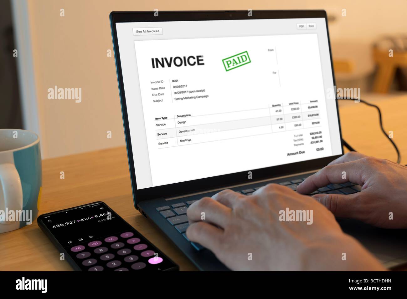 Fattura digitale con timbro a pagamento visualizzato sullo schermo del computer portatile, calcolatrice dello smartphone accanto alla tazza da caffè. Concetto di fatturazione online, gestione finanziaria, a. Foto Stock