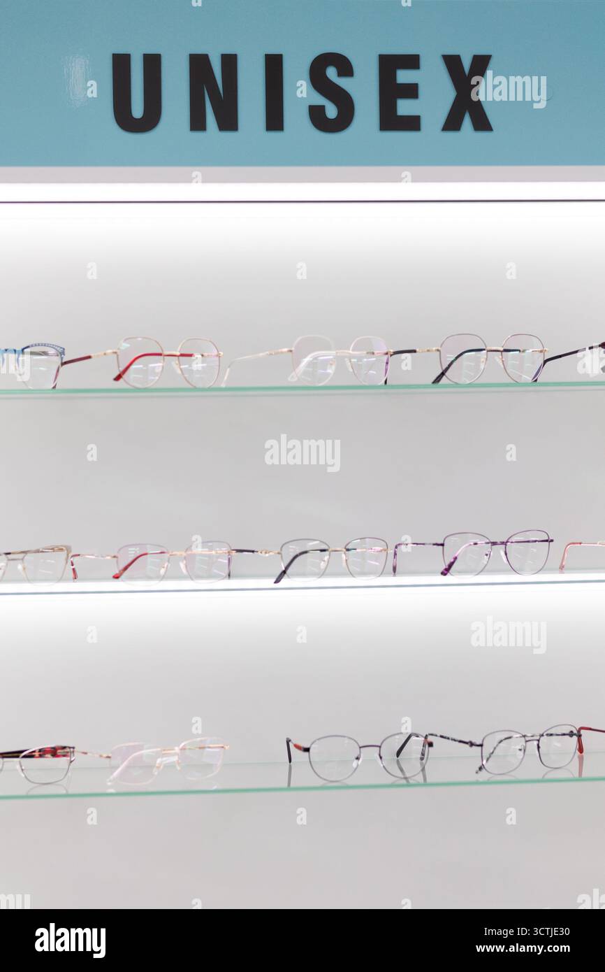 File di occhiali unisex alla moda sono disposti in modo ordinato su un elegante ripiano in un salone ottico, invitando i clienti a esplorare. Foto Stock