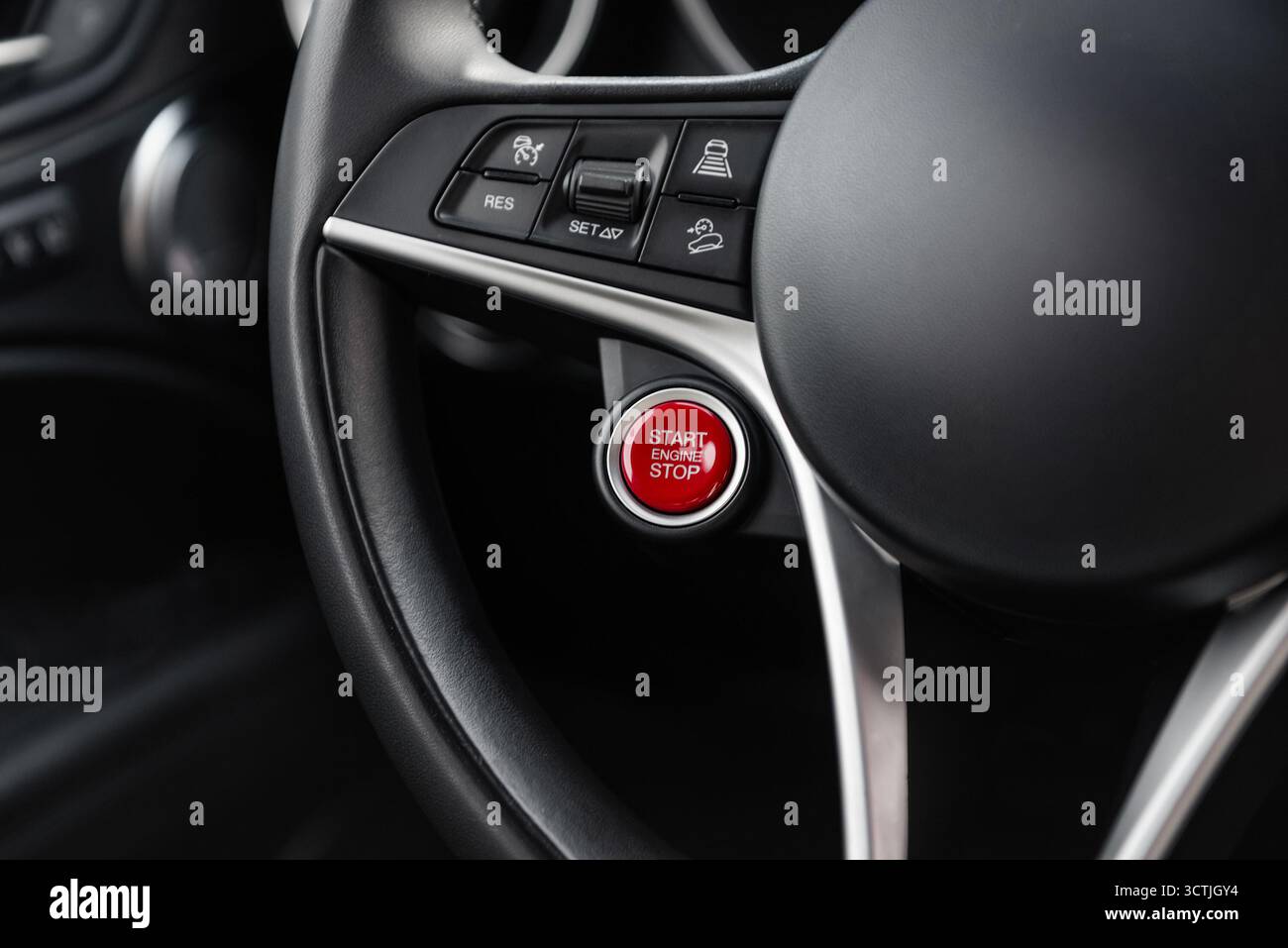 Volante dell'auto con grande pulsante rosso di avviamento del motore. Abitacolo moderno e di lusso con finiture in metallo Foto Stock