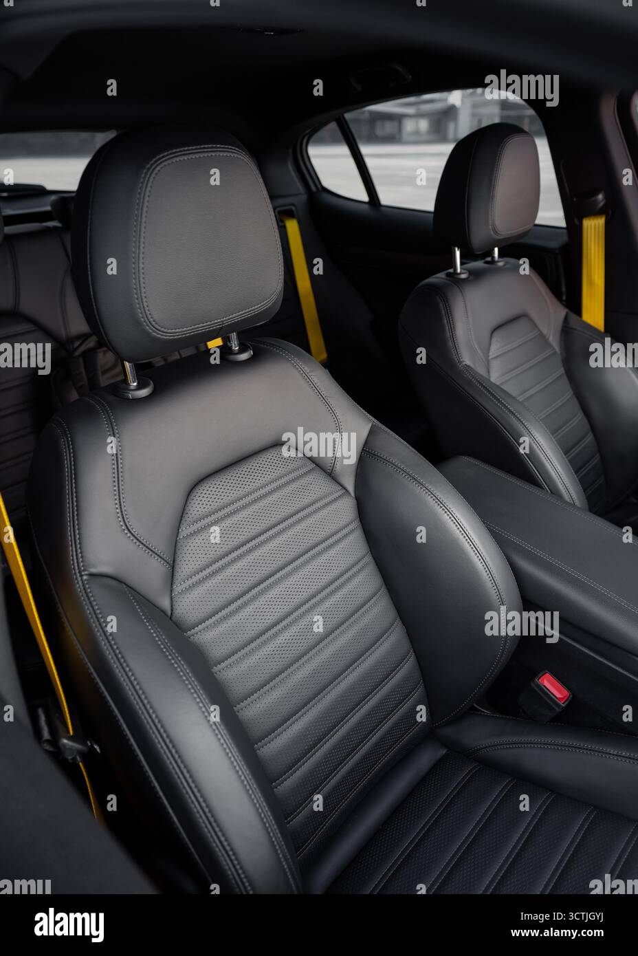Abitacolo con sedili sportivi e cinture di sicurezza gialle. Sedile anteriore in pelle di un'auto compatta in primo piano e panca posteriore sullo sfondo. Interni moderni Foto Stock