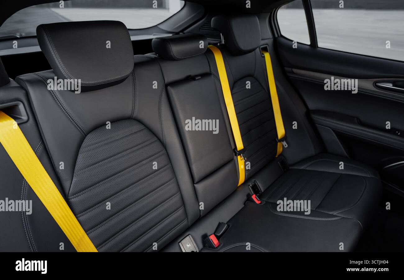 Sedili posteriori in pelle con cinture di sicurezza gialle in una vettura. Interni Hatchback o SUV in pelle nera e rivestimento padiglione. Foto Stock