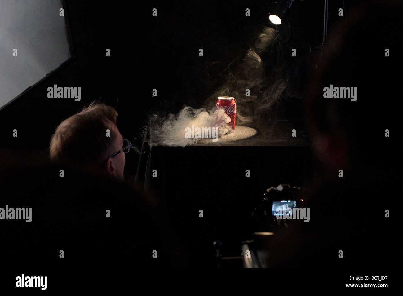 Lo scatto in studio della coca-cola può essere messo sotto i riflettori fumosi con l'operatore della fotocamera che cattura il prodotto e fotografa cinematografica commerciale Foto Stock