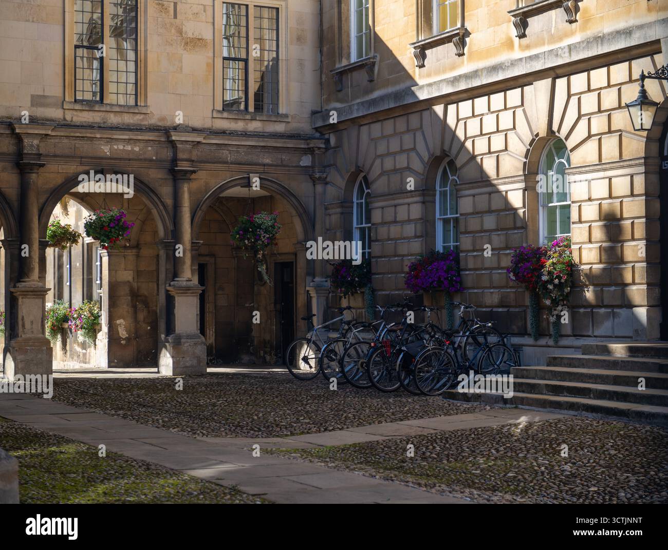 Cortile del Peterhouse College, Cambridge, con biciclette, archi in pietra e cesti di fiori appesi nel più antico college universitario d'Inghilterra Foto Stock