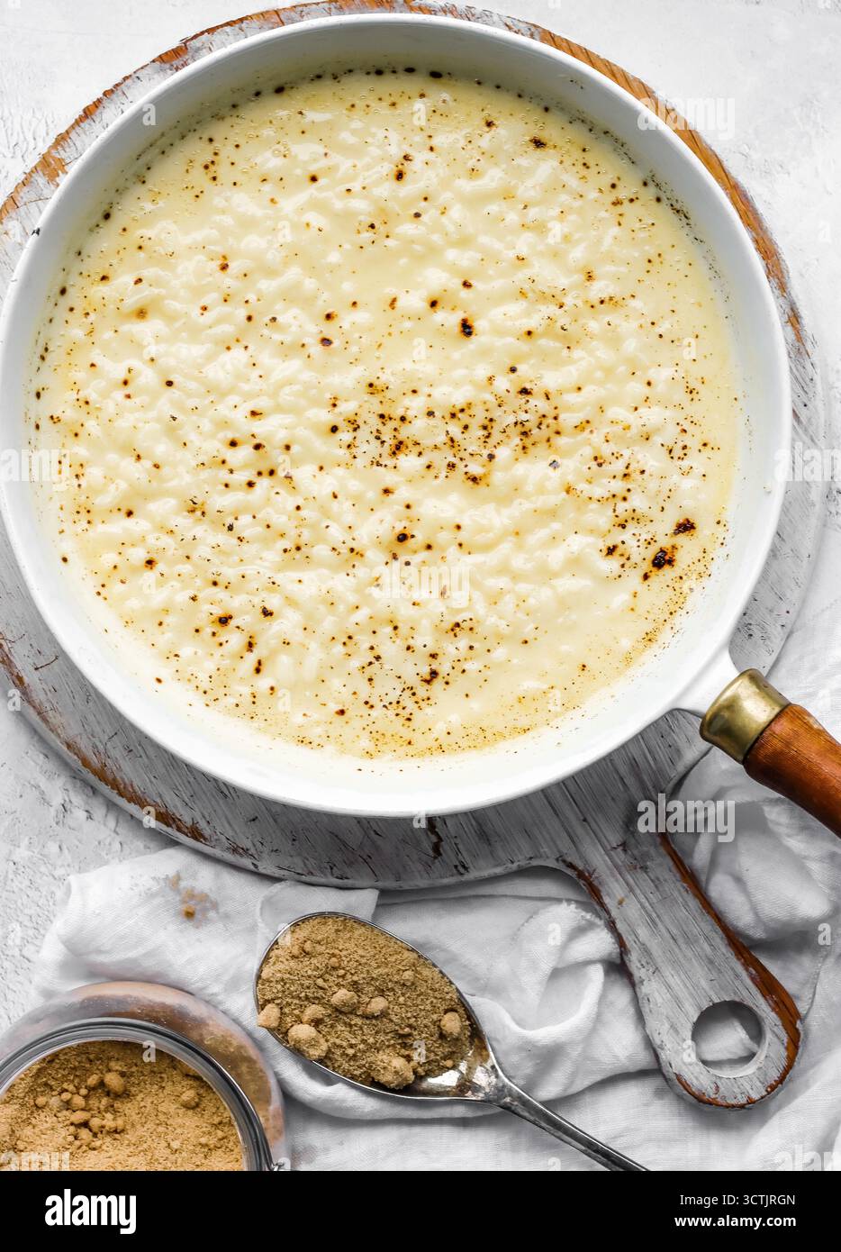 Classico budino di riso al forno con una superficie dorata e una consistenza cremosa, fotografato con luce naturale su uno sfondo bianco rustico per un dessert confortevole Foto Stock