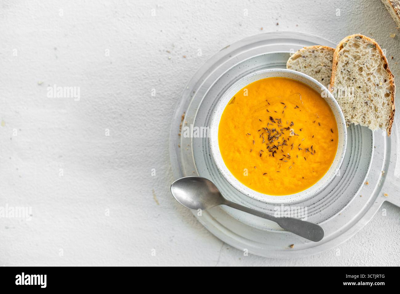 Stesa piatta di carote e zuppa di citronella con fette di pane croccante, fotografata con luce naturale soffusa su uno sfondo luminoso e ruvido. Foto Stock