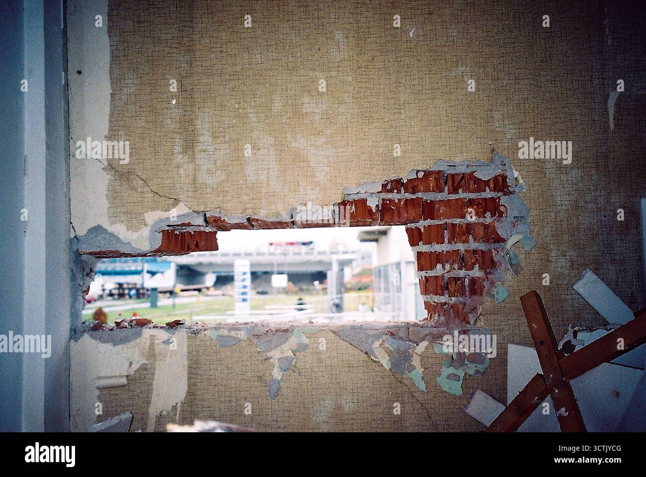 Foro quadrato nella parete esterna di una fabbrica abbandonata con carta da parati, che mostra l'esterno, catturata con una pellicola flash analogica. Foto Stock