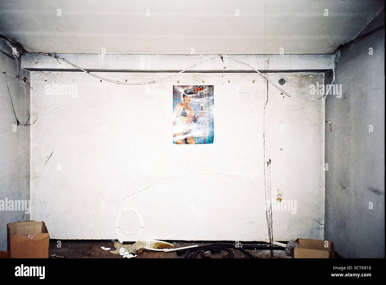 Muro bianco decaduto in una fabbrica abbandonata con un vecchio calendario con un modello di costume da bagno e pubblicità di birra, girato su film analogico. Foto Stock