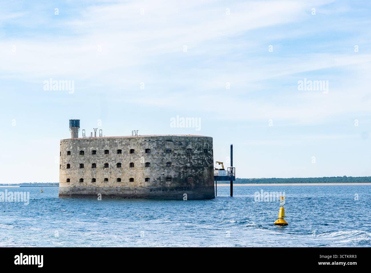Vista panoramica di Fort Boyard che si innalza dalle acque blu dell'oceano, accompagnato da un faro di navigazione giallo Foto Stock