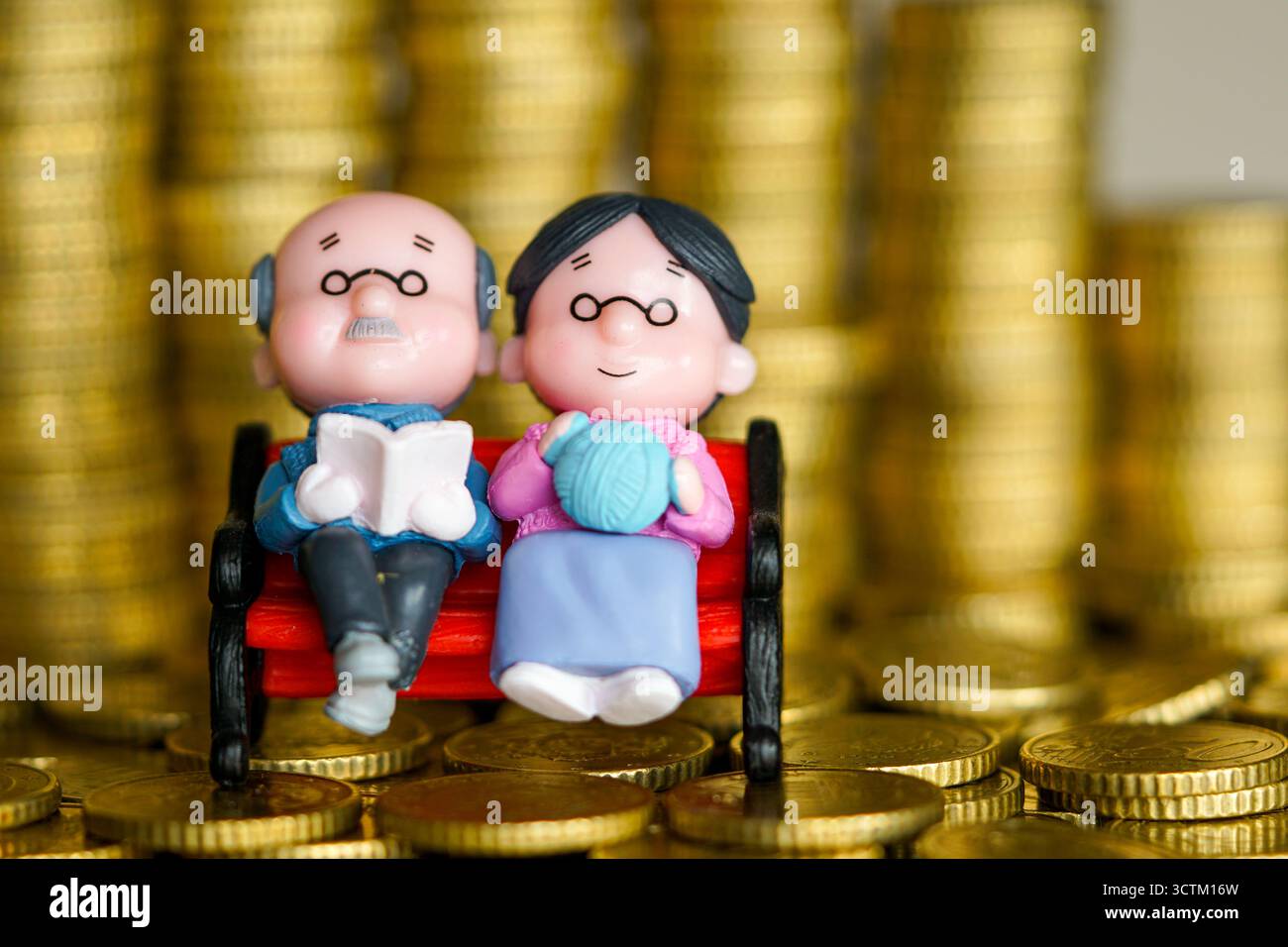 Statuette di coppia anziane in miniatura sedute sulla panchina con pile di monete d'oro, che rappresentano la pensione, i risparmi, i fondi pensione e la sicurezza finanziaria Foto Stock