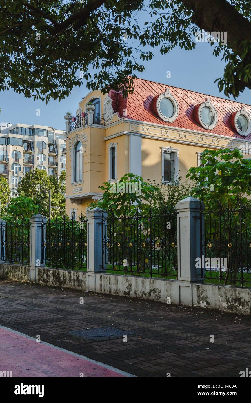 Vista di un edificio giallo con un tetto rosso, incorniciato da lussureggianti alberi verdi, si erge orgogliosamente contro un cielo limpido, Batumi, Adjara, Georgia. Foto Stock