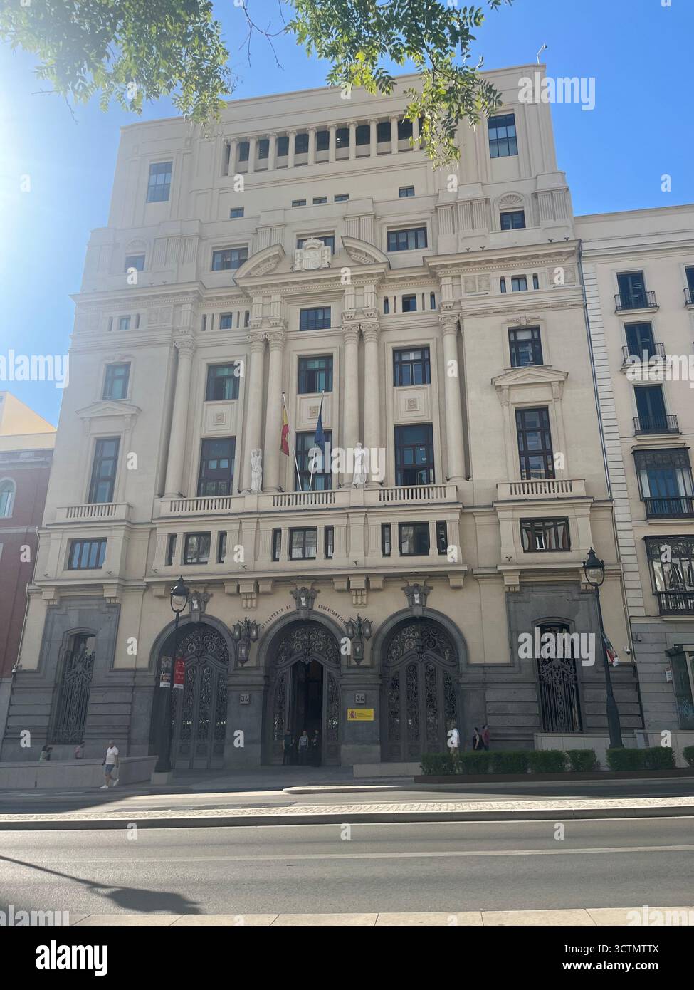 Elegante edificio neoclassico con facciata ornata, bandiere e grande ingresso nel centro di Madrid, Spagna, in una soleggiata giornata estiva. - Immagine stock catturata con smartphone