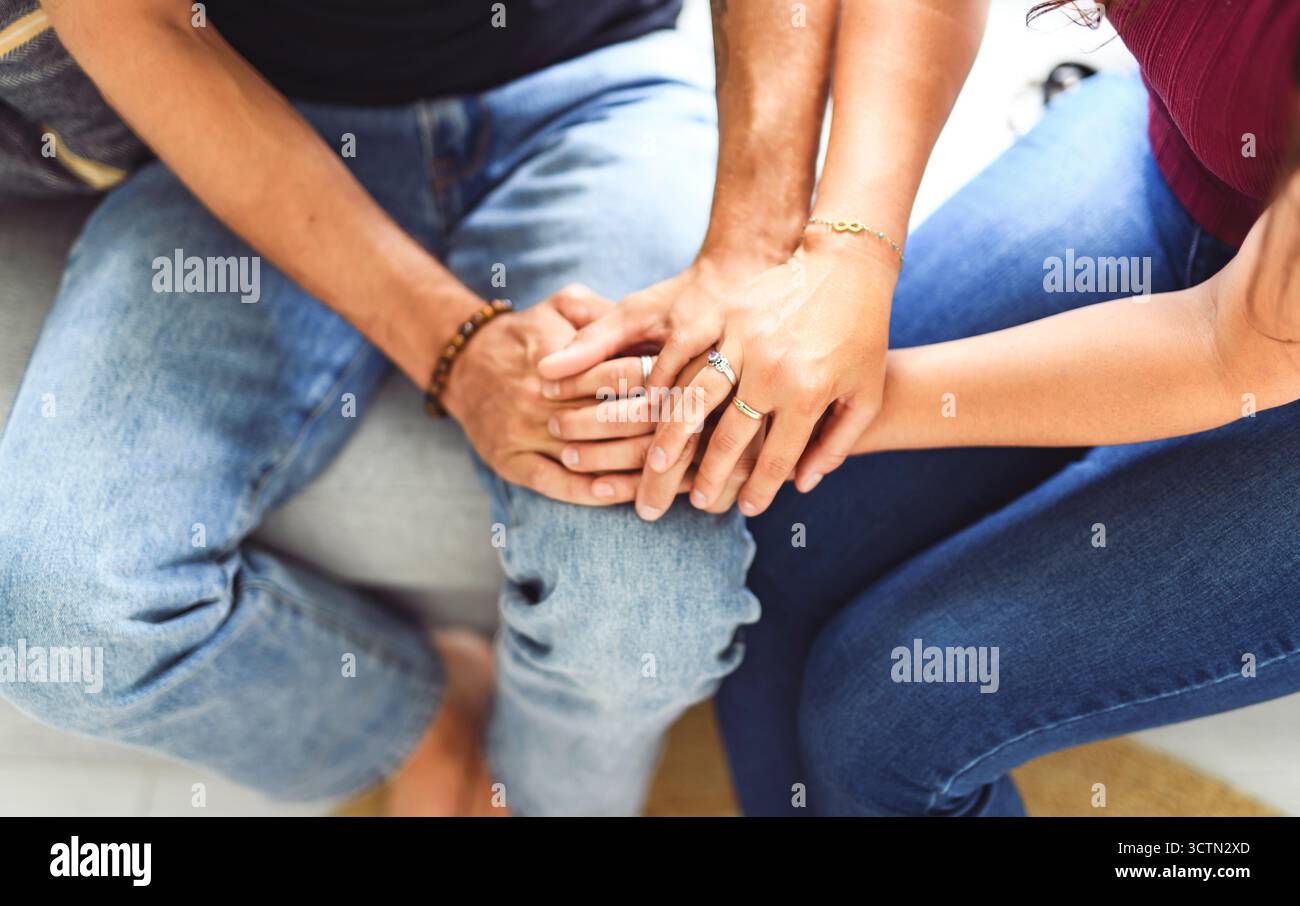 Mano nella mano attraverso esso tutto. Scatto di una coppia irriconoscibile che tiene le mani mentre si siede su un divano a casa. Foto Stock