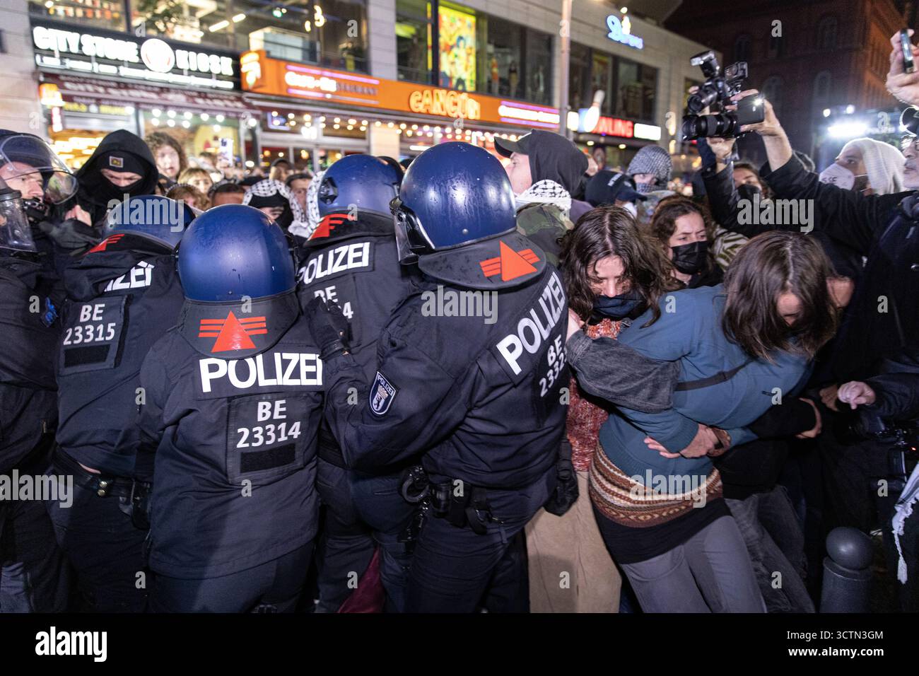 Centinaia di manifestanti filo-palestinesi si sono riuniti nei pressi della Fontana di Nettuno presso Alexanderplatz nel centro di Berlino martedì 7 ottobre 2025, nonostante il divieto della polizia alla manifestazione, in occasione del secondo anniversario degli attacchi terroristici di Hamas contro Israele. I partecipanti hanno cantato slogan come "Gloria alla resistenza", "Intifada fino alla vittoria" e "dal fiume al mare, la Palestina sarà libera”. Gli scontri scoppiarono quando gli ufficiali si trasferirono per disperdere il raduno, portando a numerosi arresti e scontri. La scena è diventata tesa e caotica mentre i manifestanti resistevano agli ordini della polizia. Il momento del rally o Foto Stock Centinaia di manifestanti filo-palestinesi si sono riuniti nei pressi della Fontana di Nettuno presso Alexanderplatz nel centro di Berlino martedì 7 ottobre 2025, nonostante il divieto della polizia alla manifestazione, in occasione del secondo anniversario degli attacchi terroristici di Hamas contro Israele. I partecipanti hanno cantato slogan come "Gloria alla resistenza", "Intifada fino alla vittoria" e "dal fiume al mare, la Palestina sarà libera”. Gli scontri scoppiarono quando gli ufficiali si trasferirono per disperdere il raduno, portando a numerosi arresti e scontri. La scena è diventata tesa e caotica mentre i manifestanti resistevano agli ordini della polizia. Il momento del rally o Foto Stock