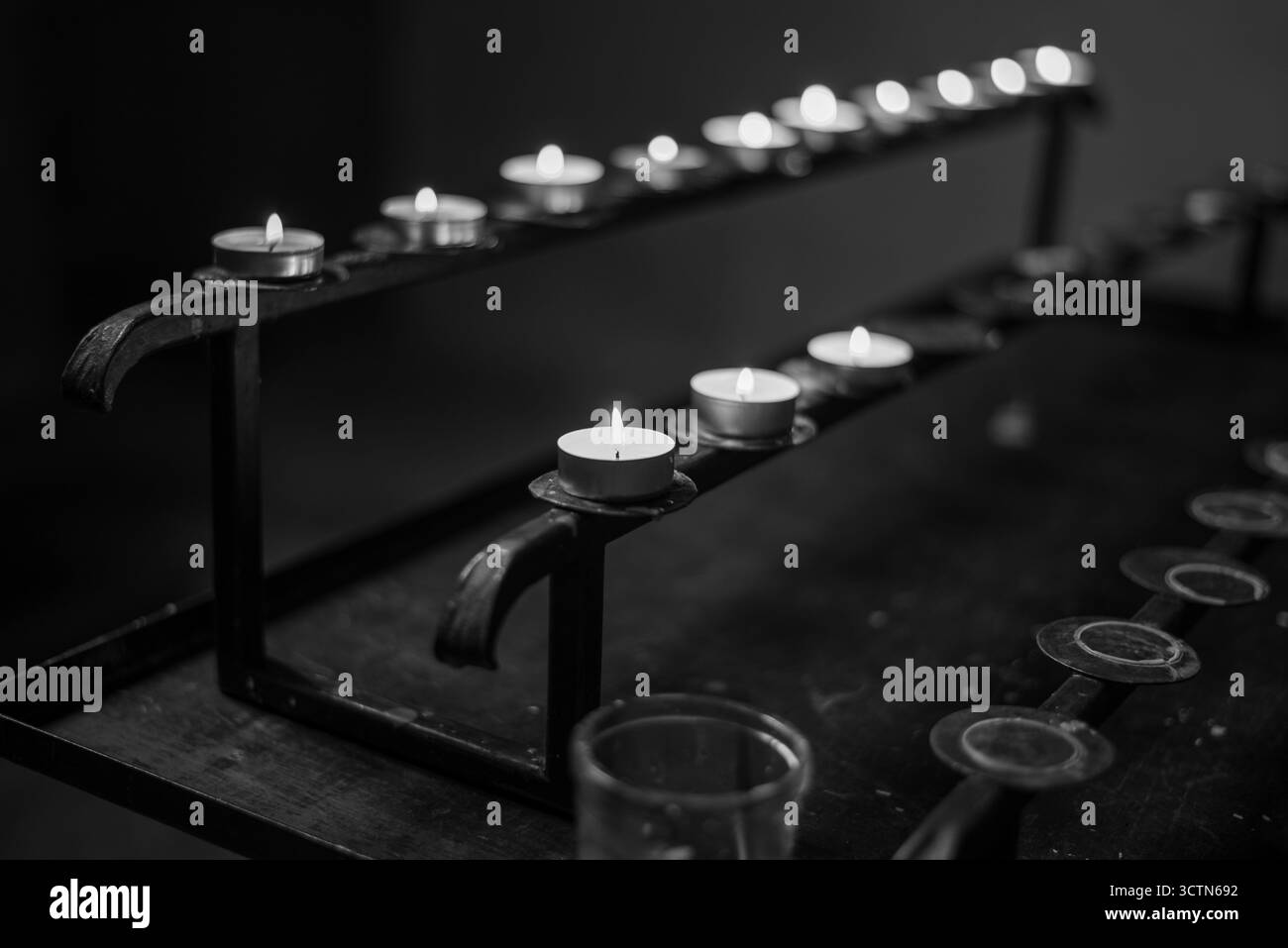 Foto in bianco e nero di candele luminose su un piedistallo in metallo. Foto Stock