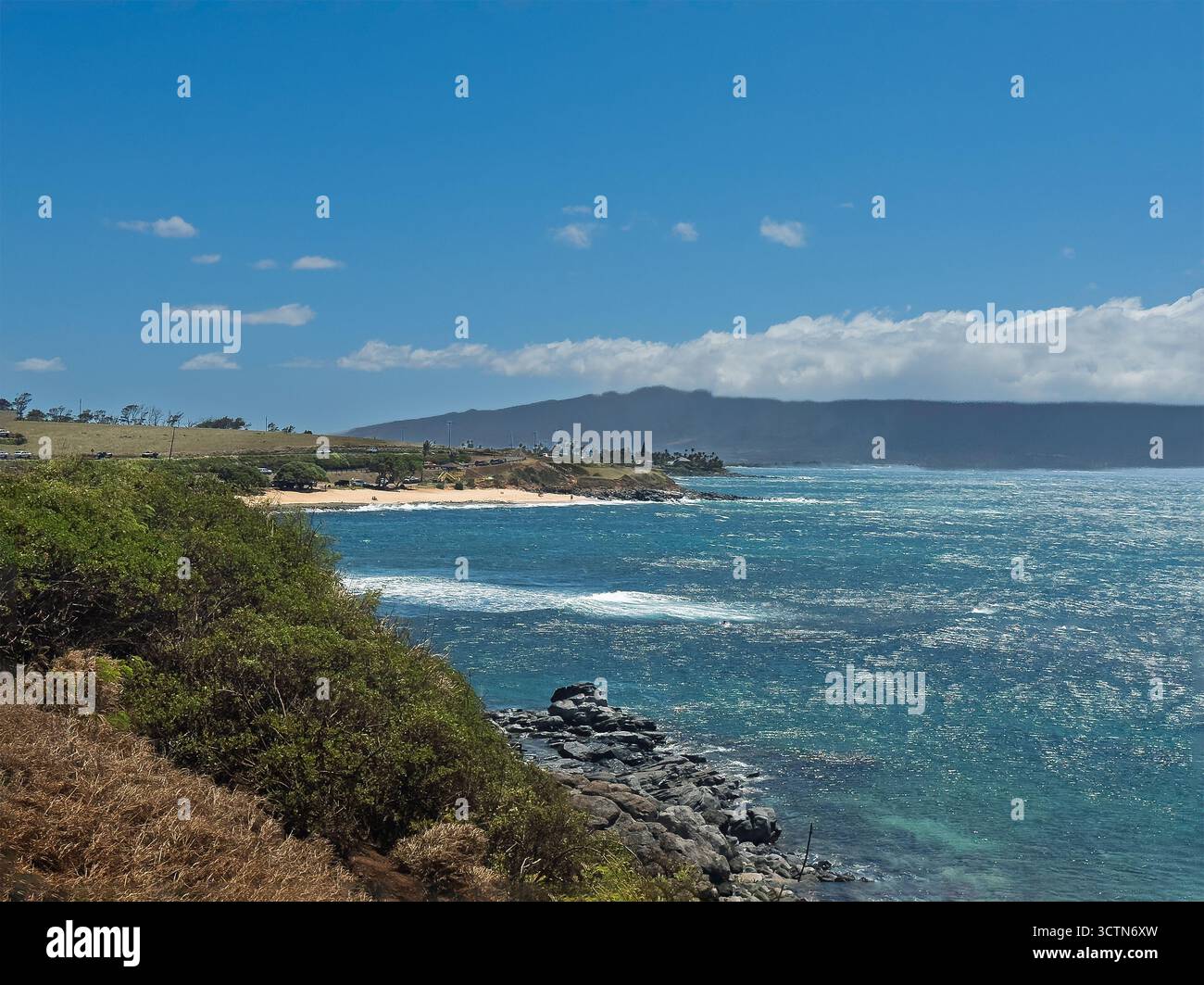Paia, Maui, Hawaii, USA - 13 luglio 2025: Ho'okipa Beach Park. Rocce laviche nere nel surf dell'oceano. Spiaggia sabbiosa sul lato opposto. Montagna sull'horizo Foto Stock