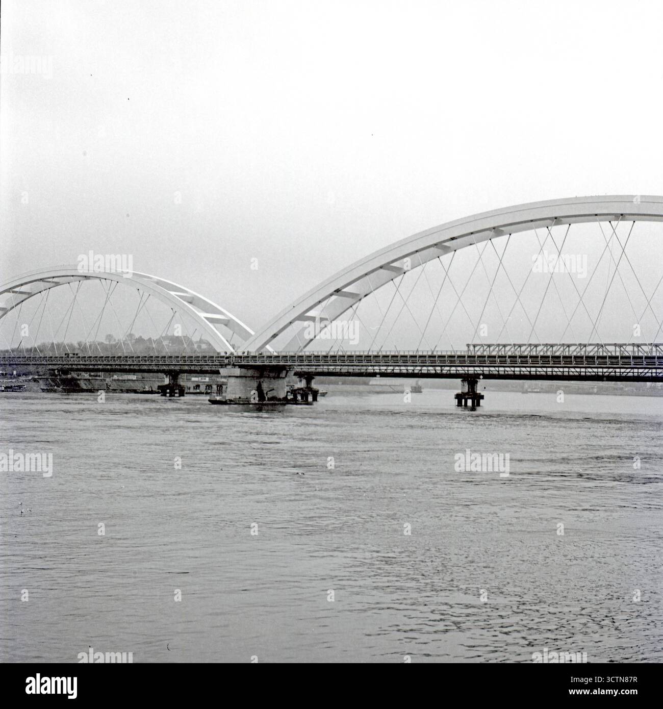 Costruzione intermedia Žeželjev Bridge, archi centrati nel telaio sotto cieli nuvolosi, catturati in stile analogico con una forte prospettiva strutturale. Foto Stock
