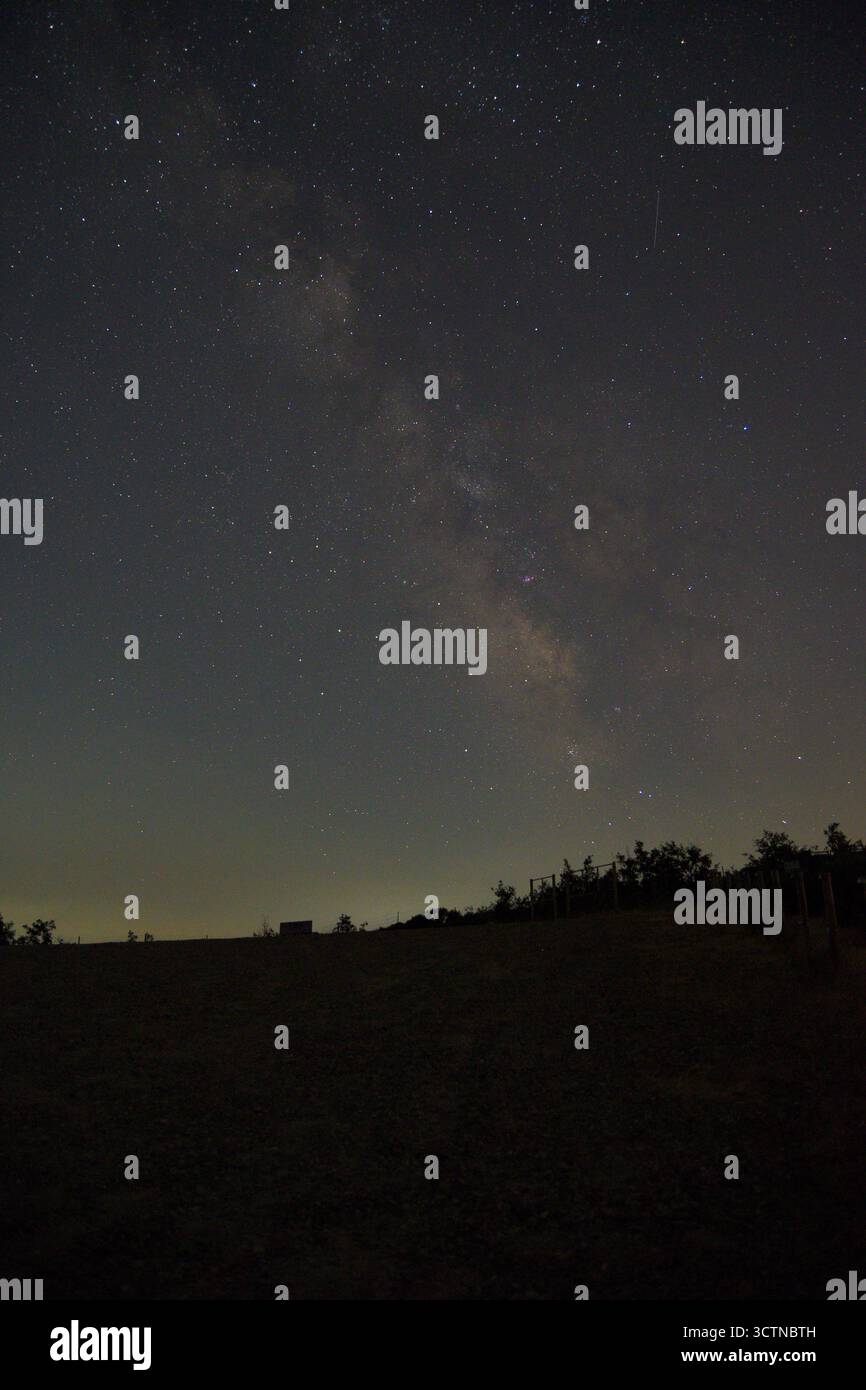 Cielo stellato notturno con la via Lattea visibile sopra un paesaggio rurale scuro. Visuale chiara di innumerevoli stelle e fasce di polvere cosmiche, catturate in condizioni di scarsa illuminazione Foto Stock
