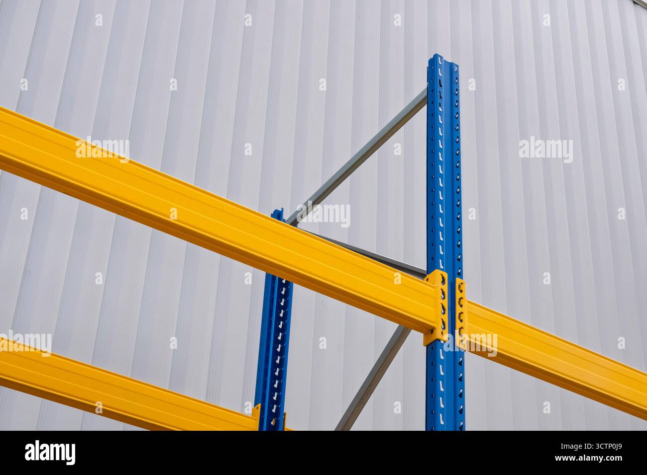 Sistema di scaffalatura per magazzini industriali con travi gialle e montanti blu. Vista ravvicinata dello sfondo bianco ondulato della parete. Gli scaffali per impieghi pesanti hanno usato i Foto Stock