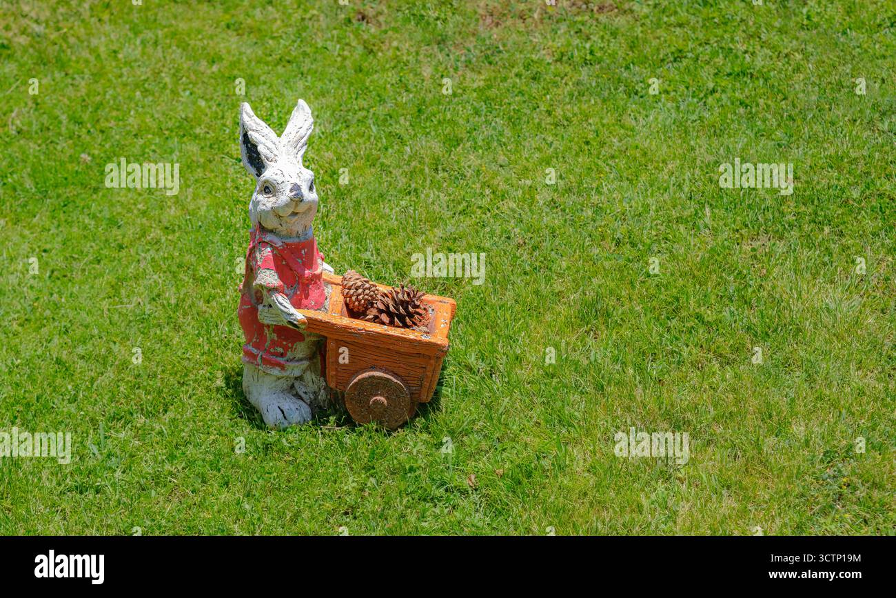 Stravagante statua del giardino di conigli con carriola. Questa decorazione giocosa aggiunge un tocco di fantasia al giardino. Perfetto per temi legati al giardinaggio a. Foto Stock