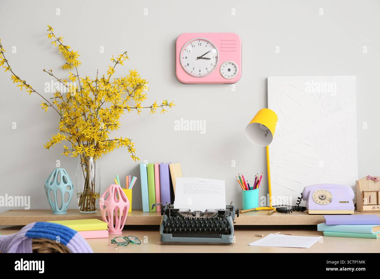 Postazione di lavoro con lampada e macchina da scrivere sul tavolo vicino alla parete bianca della stanza Foto Stock