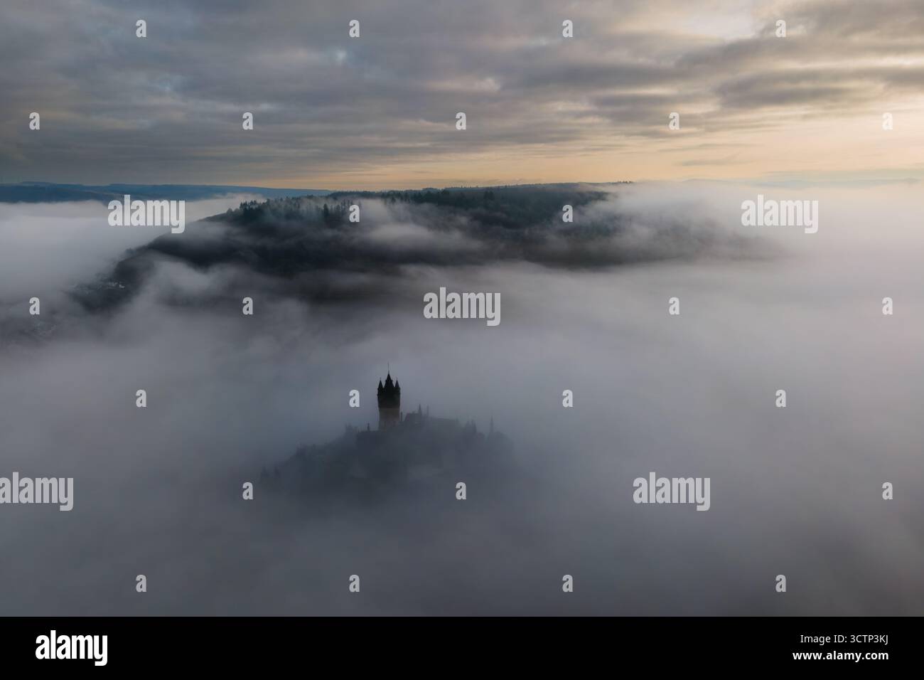 Ampia vista aerea del castello di Cochem che si apre parzialmente attraverso basse nuvole all'alba, con foreste circostanti e un cielo spettacolare Foto Stock