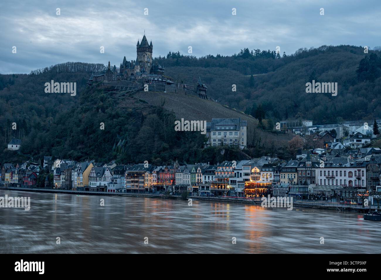 Foto a lunga esposizione del fiume Mosella con riflessi d'acqua soffici, una città Cochem parzialmente illuminata e il castello arroccato sulla cima di una collina Foto Stock