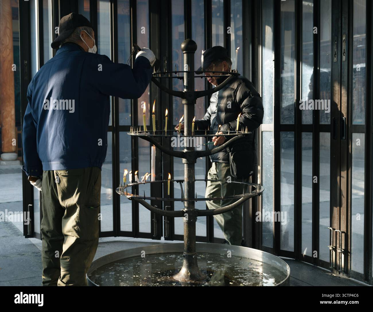 Il lavoratore del tempio di Osaka pulisce con cura il supporto delle candele dopo che le fiamme si sono bruciate e la luce soffusa viene filtrata attraverso un involucro di vetro Foto Stock
