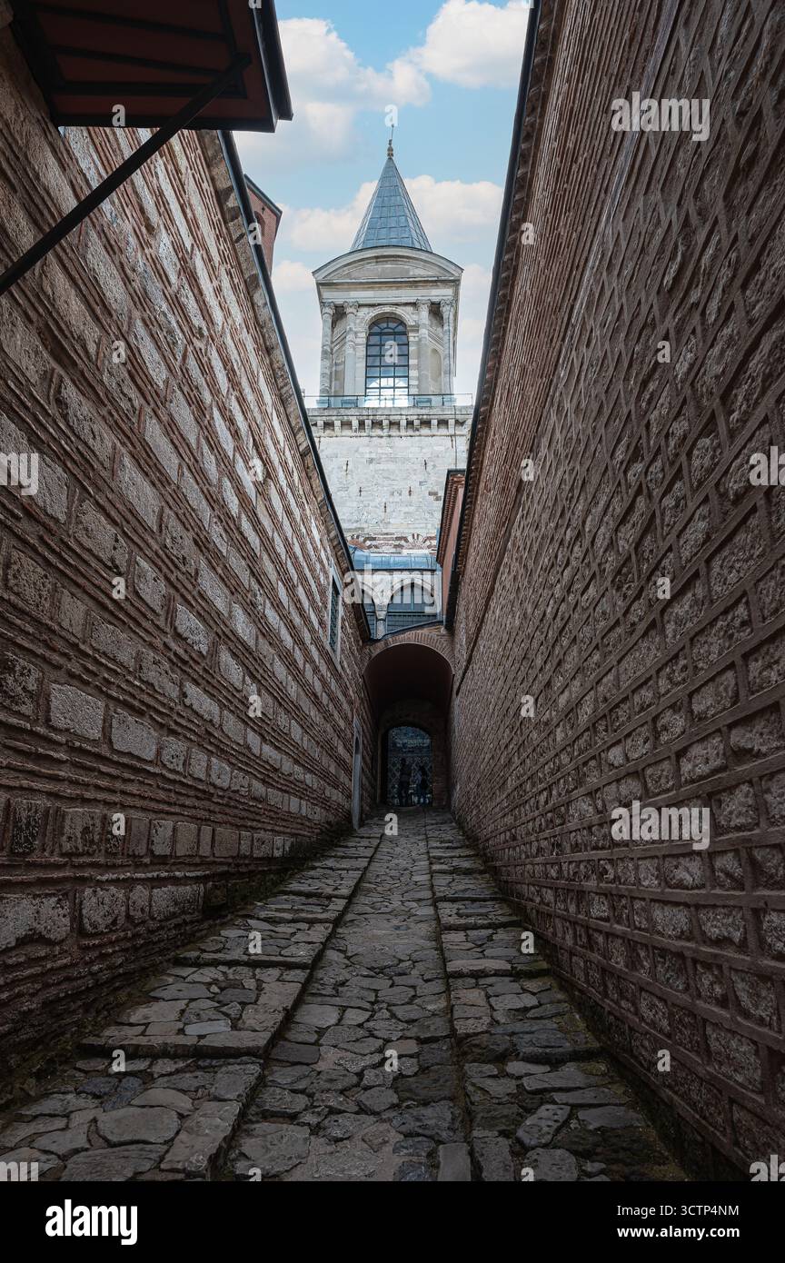 Uno stretto vicolo nel Palazzo Topkapi, Istanbul, Turchia, conduce verso una torre storica, catturando il fascino e la profondità dell'architettura del palazzo Foto Stock