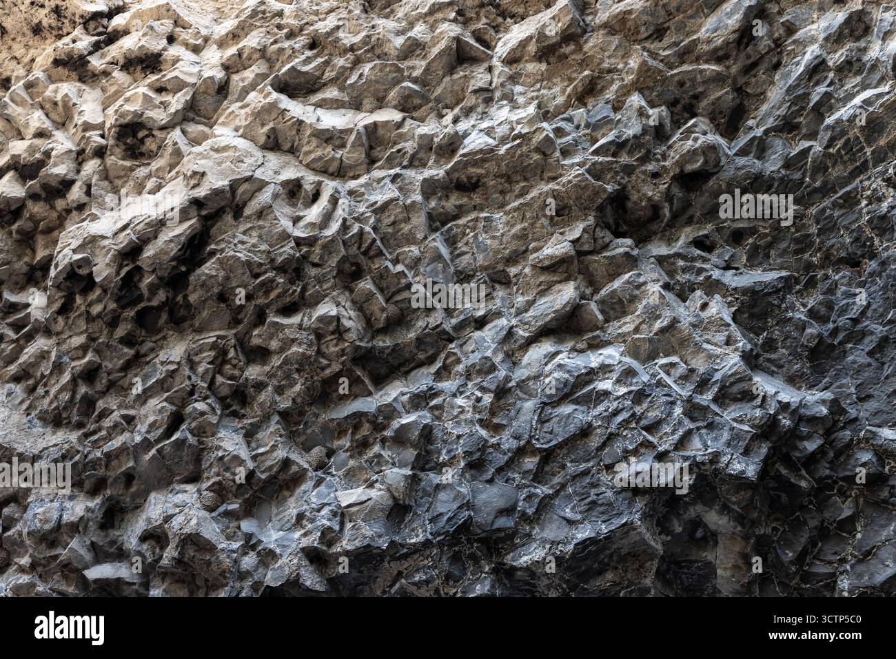 Primo piano di una parete rocciosa ruvida e scoscesa che mostra texture e tonalità naturali Foto Stock