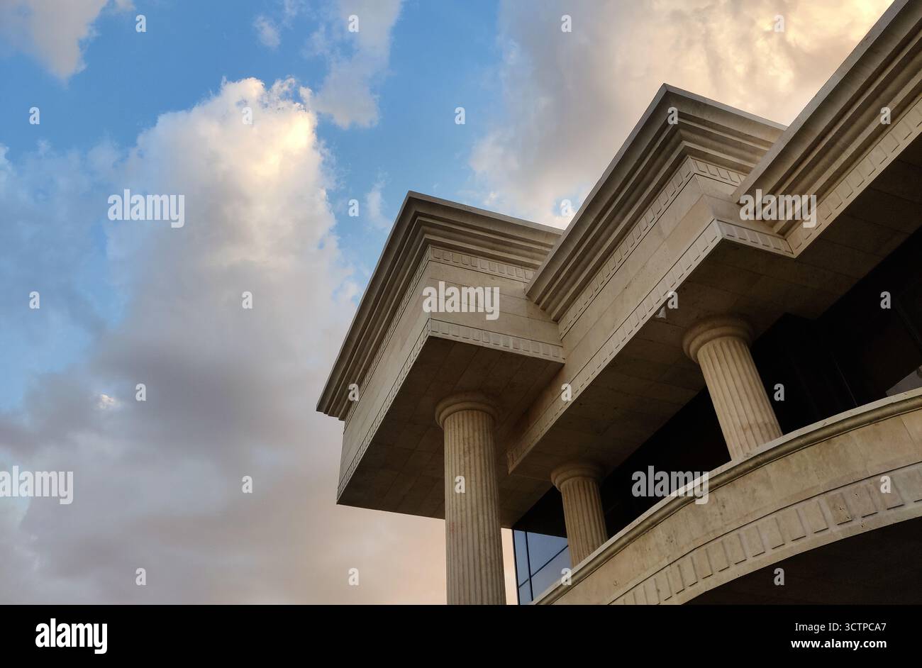 Una vista dall'angolo basso mette in risalto le maestose colonne e gli intricati dettagli di un edificio classico. La struttura è incorniciata da un cielo vibrante e da nuvole spettacolari. Foto Stock