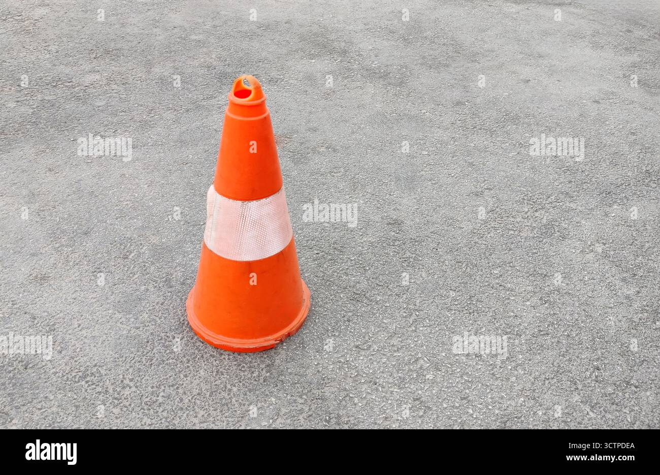 Vecchio cono arancione in piedi su strada asfaltata. Il marcatore di sicurezza con banda riflettente viene utilizzato per l'avvertenza, il controllo e la guida nella costruzione. Foto Stock
