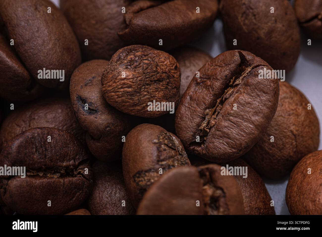 Primo piano in chicchi di caffè tostati. Macinatura di chicchi di caffè tostati che ne evidenziano le ricche tonalità di marrone, le superfici ruvide e gli oli naturali. Foto Stock