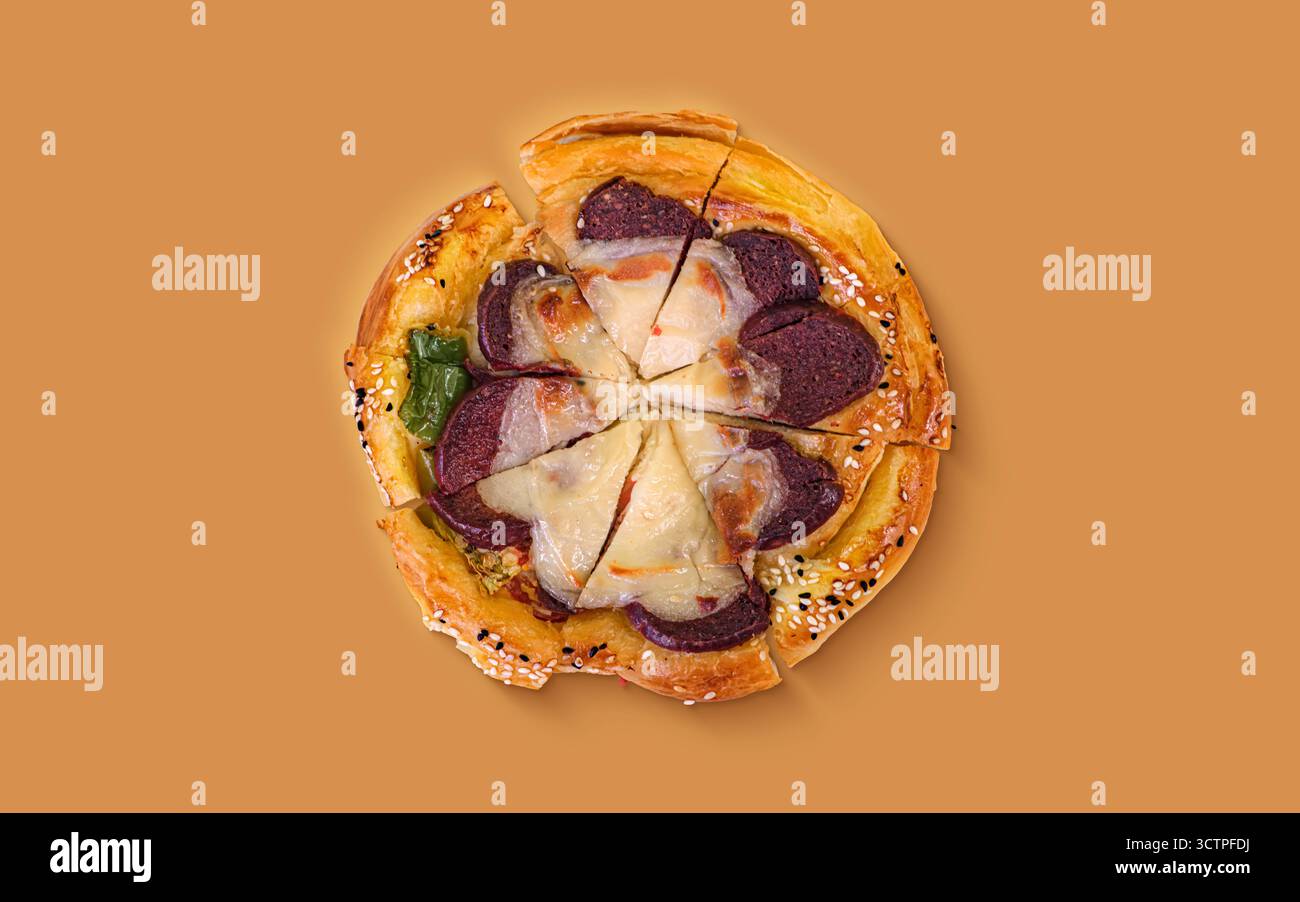 Vista dall'alto della mini pizza di pasticceria cotta con formaggio fuso, fette di salsiccia e semi di sesamo sulla crosta. L'esclusiva torta rotonda viene tagliata a fette. Foto Stock