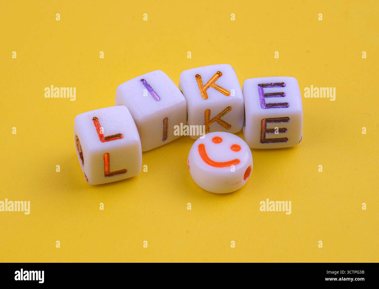 Cubi bianchi con colorate lettere incise che scrivono "COME", posizionati su uno sfondo giallo brillante. Accompagnato da una perla con una faccia sorridente arancione. Foto Stock