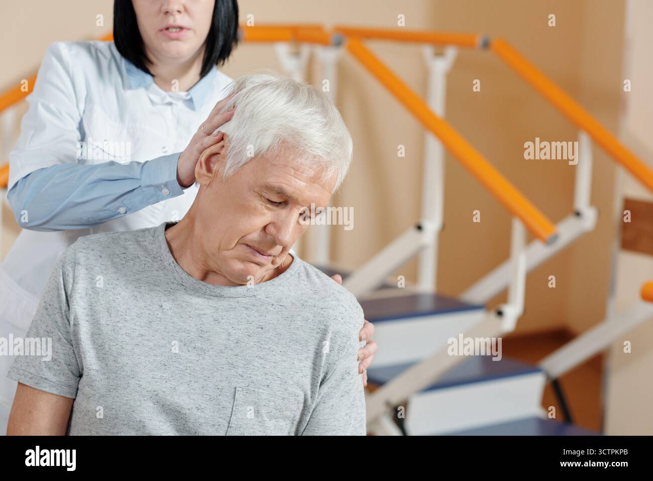 Terapeuta femminile professionale che dà un massaggio paziente maschile caucasico maturo nel centro di riabilitazione Foto Stock