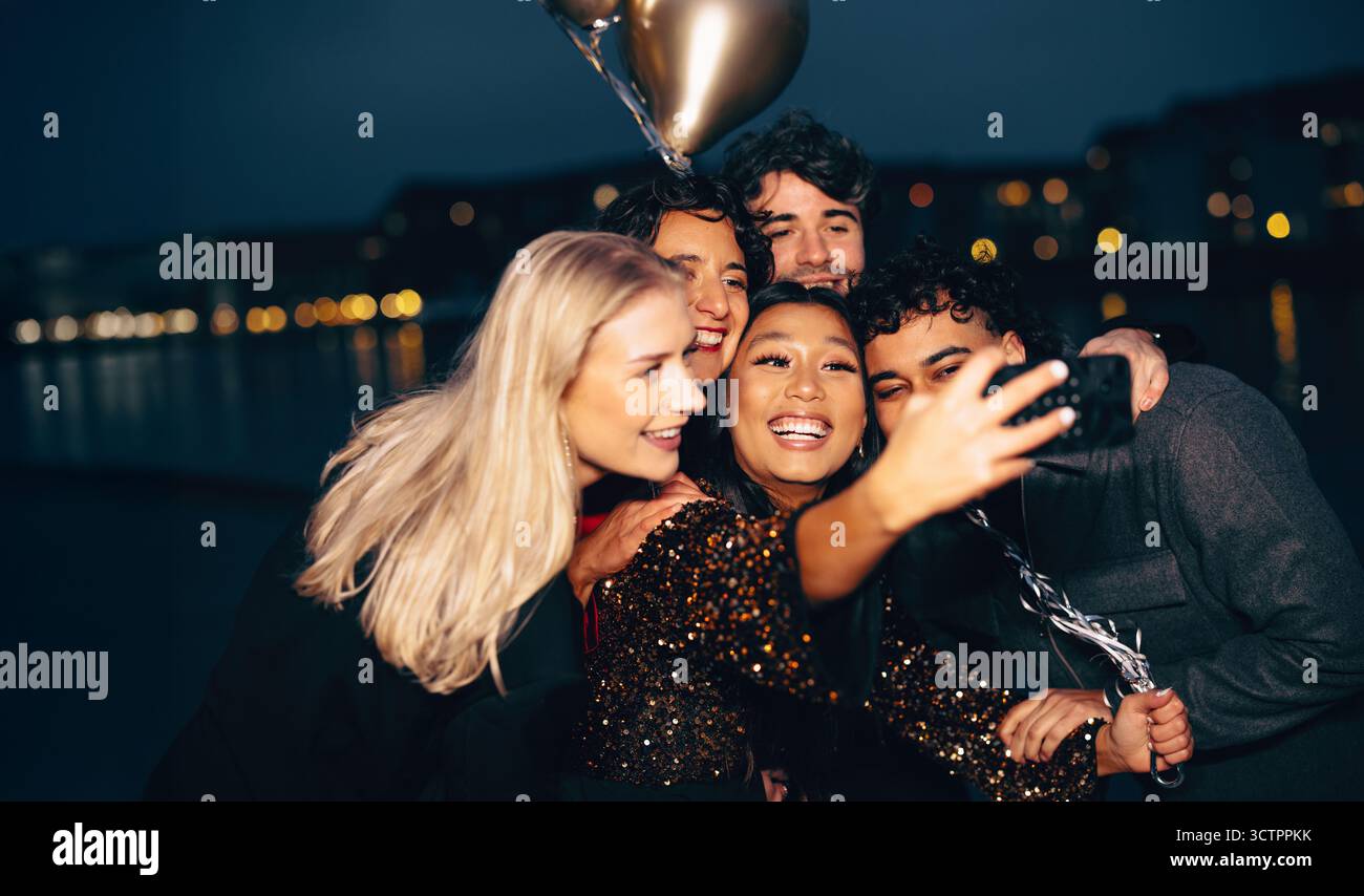 Un gruppo di amici allegri che scattano un selfie all'aperto di notte, illuminato dalle luci della città. Foto Stock Un gruppo di amici allegri che scattano un selfie all'aperto di notte, illuminato dalle luci della città. Foto Stock